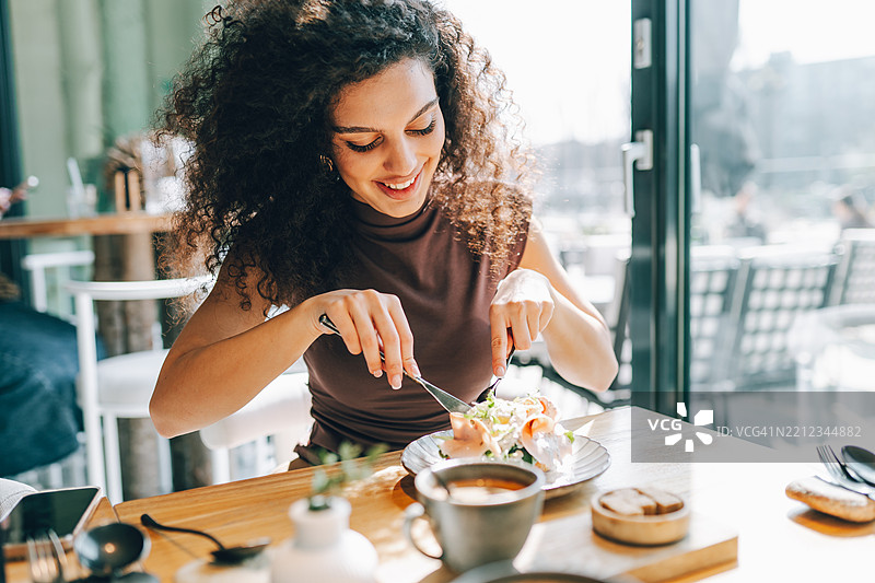 年轻女性在现代餐厅享用健康餐。图片素材