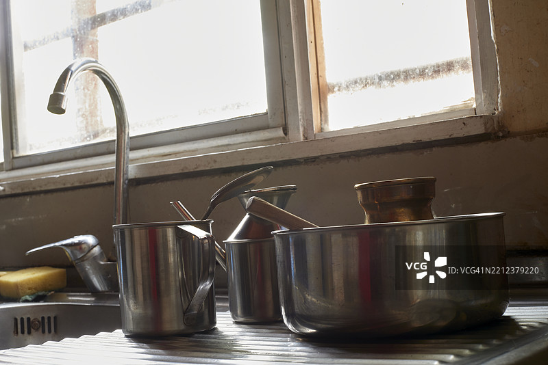金属炊具和厨房工具整齐地摆放在水槽旁,柔和的阳光照亮了晾干的器具,营造出温暖有序的烹饪空间。图片素材