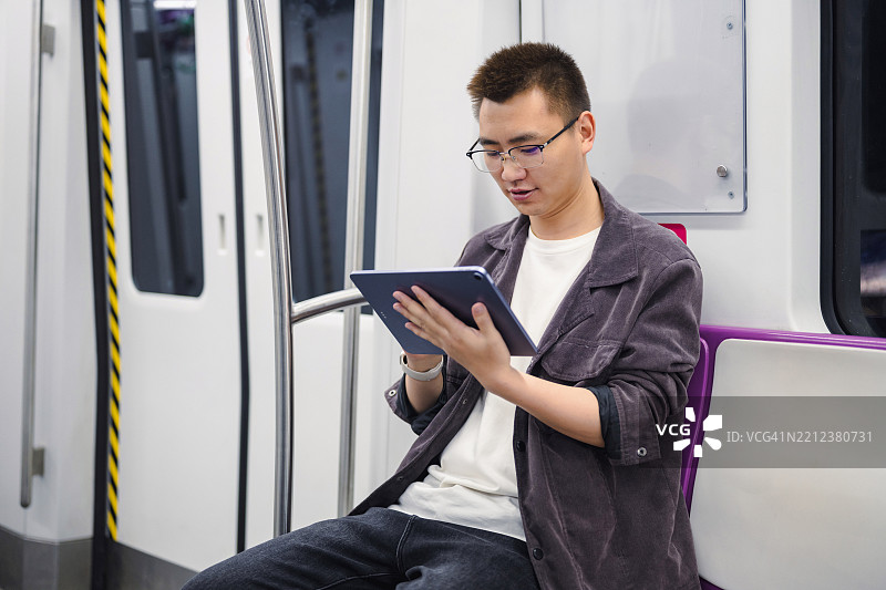 年轻男子坐在地铁上使用iPad图片素材