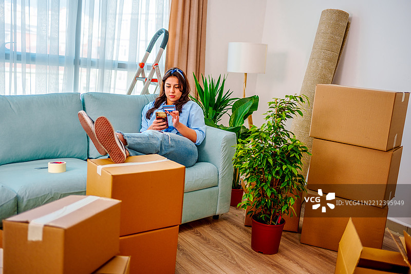 年轻女性正在用手机和信用卡购物和下单，准备搬入新家。图片素材