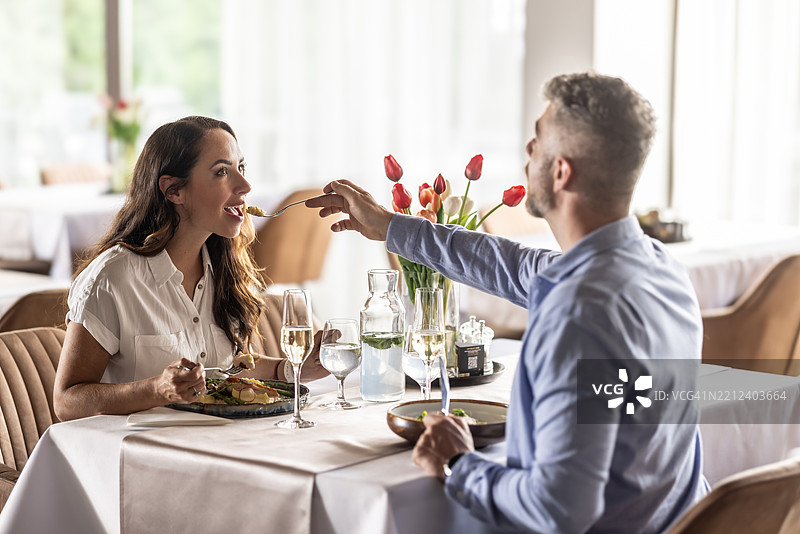 一对年轻情侣享受着浪漫的双人晚餐，他们品尝着对方的食物。图片素材