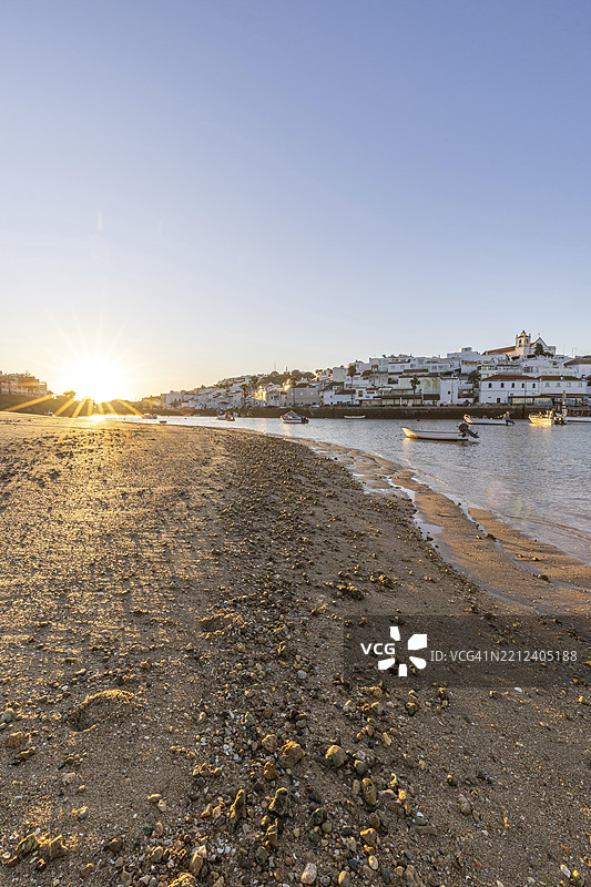 大西洋的日出，渔村的天际线在港口后面。黎明时分的沙滩风景照片，拍摄于葡萄牙阿尔加维的波尔蒂芒费拉古杜。图片素材