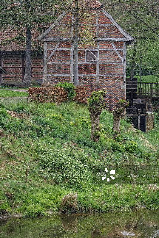 一座古老的半木结构房屋，旁边有一座磨坊，四周被绿色植被环绕，弗雷登，明斯特兰，德国图片素材