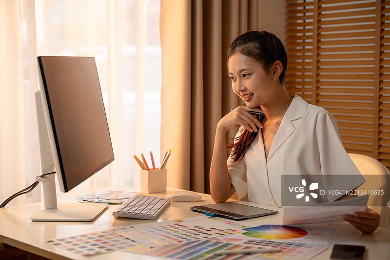 年轻的亚洲女性平面设计师在记录标志设计的笔记。平面设计师在笔记本电脑上工作，并使用图形绘图笔。图片素材