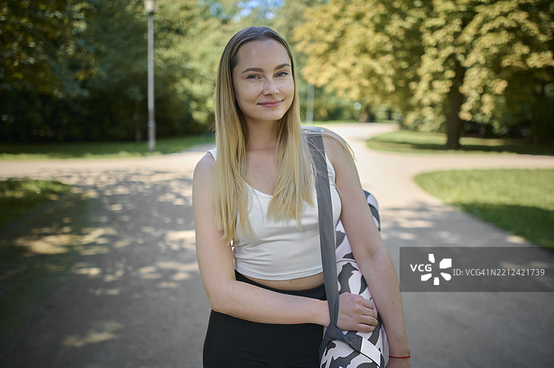 自信活跃的女性在公园里携带瑜伽垫的肖像图片素材