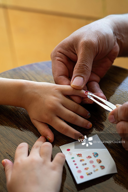 父亲在小女孩的手上贴上五彩缤纷的指甲贴纸，享受在家的美好时光图片素材