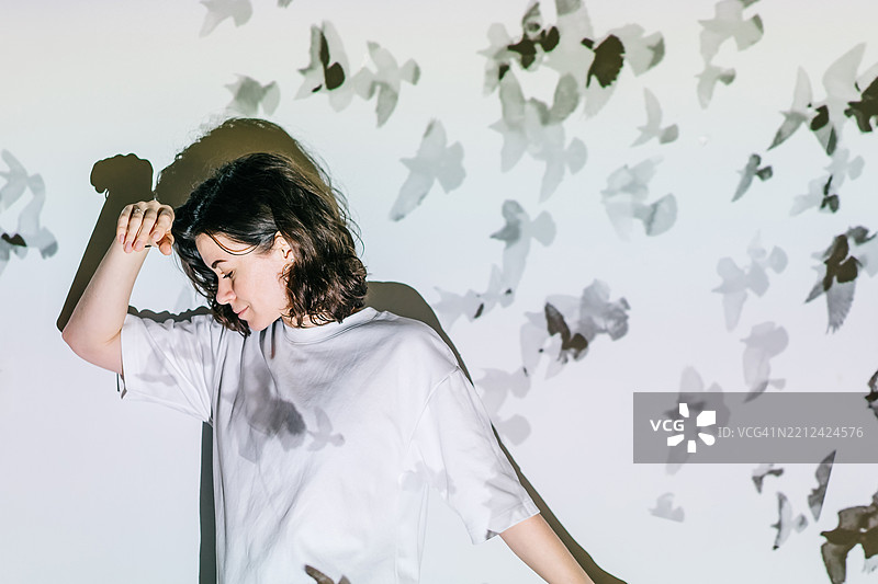 一位女性梦幻者站在白色墙壁前，墙上和她身上投影着飞翔的鸟儿。图片素材