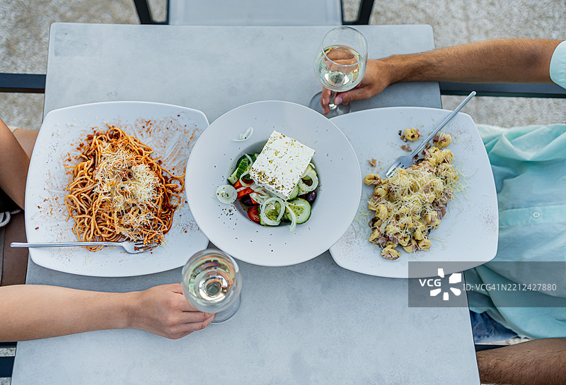 朋友们享用意大利面和希腊沙拉的午餐，手中举着白葡萄酒杯图片素材