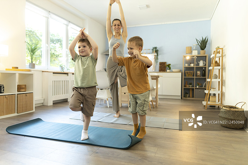 微笑快乐的男孩们在客厅里和妈妈一起锻炼，做树式瑜伽练习。图片素材
