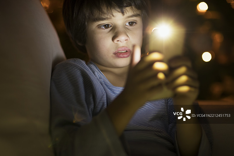 孩子在温馨昏暗的环境中使用智能手机图片素材