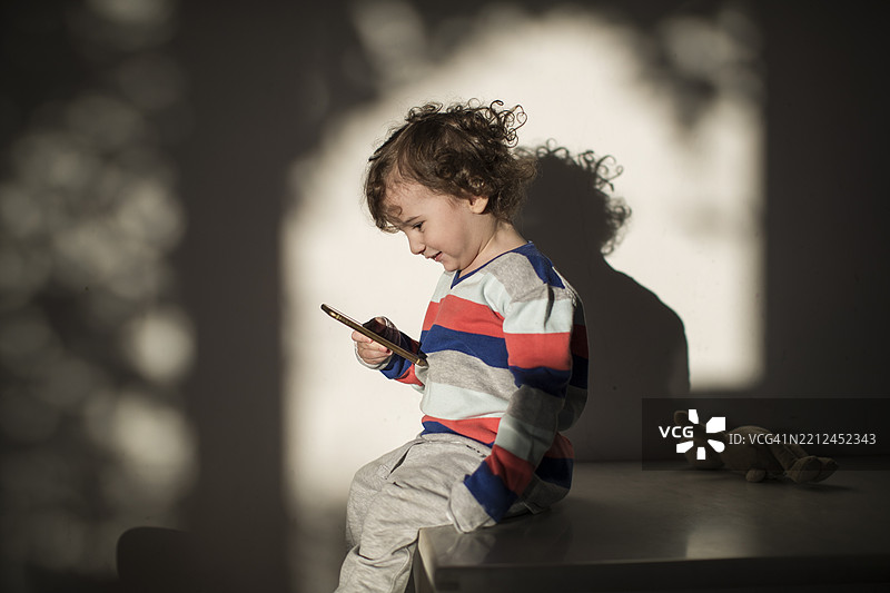 小孩在柔和的阳光下享受使用智能手机的时光图片素材