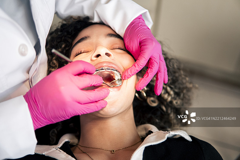 牙医在牙科诊所检查戴着牙套的年轻女性的牙齿图片素材