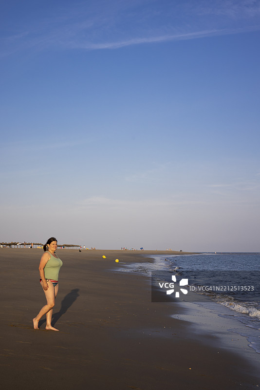 西班牙卡内拉岛海滩的女性游客沿海岸线散步图片素材