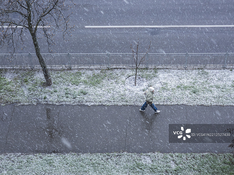 冬日里，雪花覆盖着街道，一位身影在 sidewalk 上漫步。图片素材