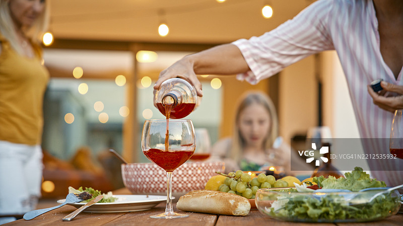 女人在露台上为家庭晚餐倒红酒入杯图片素材