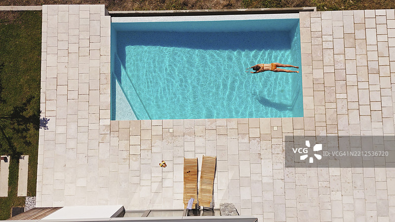 年轻女性在夏季假期中放松，漂浮在碧绿色的游泳池中图片素材