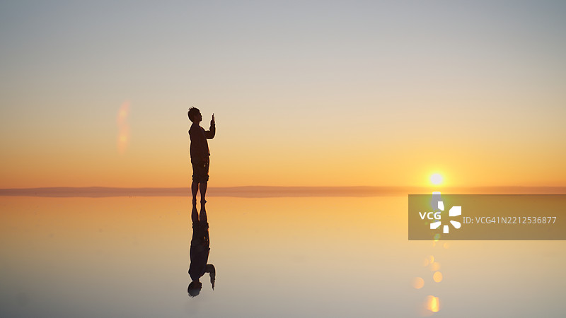 独自旅行的男子站在浅水面上，捕捉自然中的日落景象图片素材