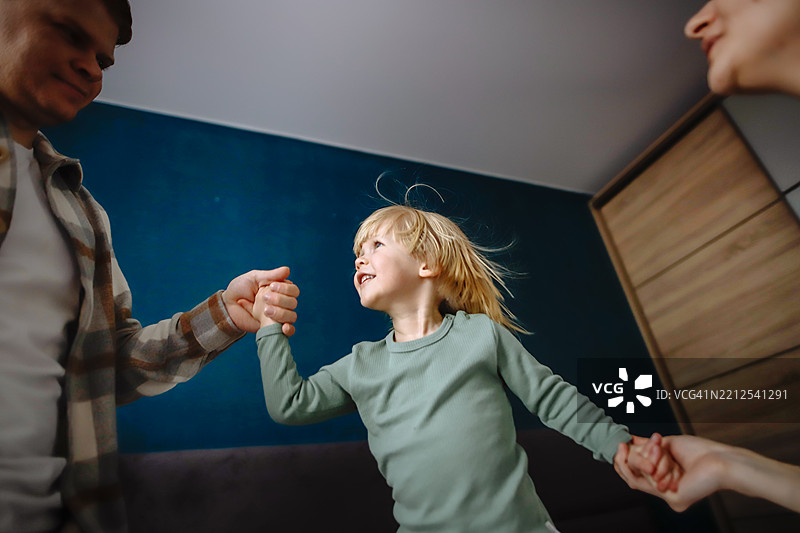 充满活力的家庭早晨：孩子快乐地跳跃，怀孕的母亲和父亲在旁，象征着爱、兴奋和期待新生命的美好。图片素材