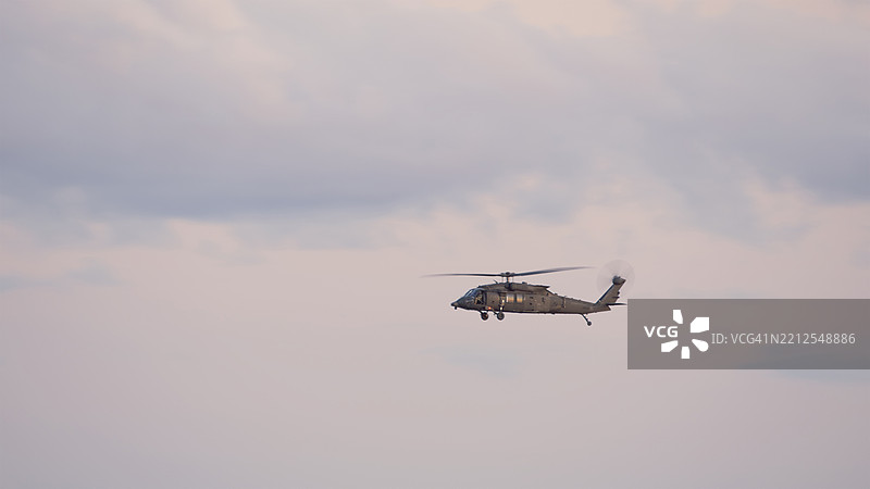 在阴云密布的天空中，军用直升机飞行，柔和的光线和多云的背景。图片素材