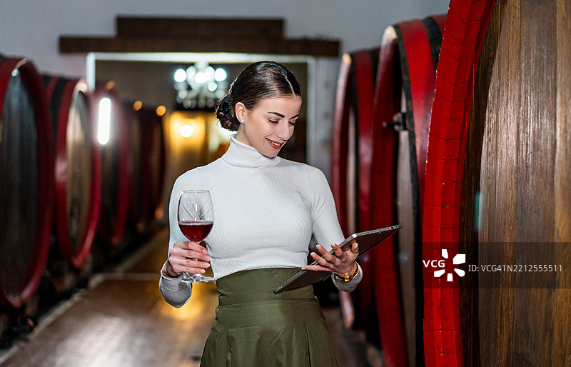 女人在酒窖里拿着玻璃杯并使用平板电脑图片素材