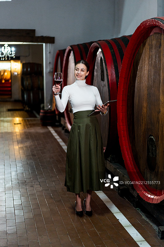 女人在酒窖里手持玻璃杯和平板电脑图片素材
