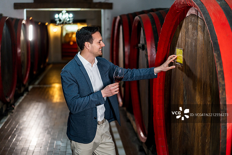 男子在酒窖中品尝橡木桶里的葡萄酒图片素材