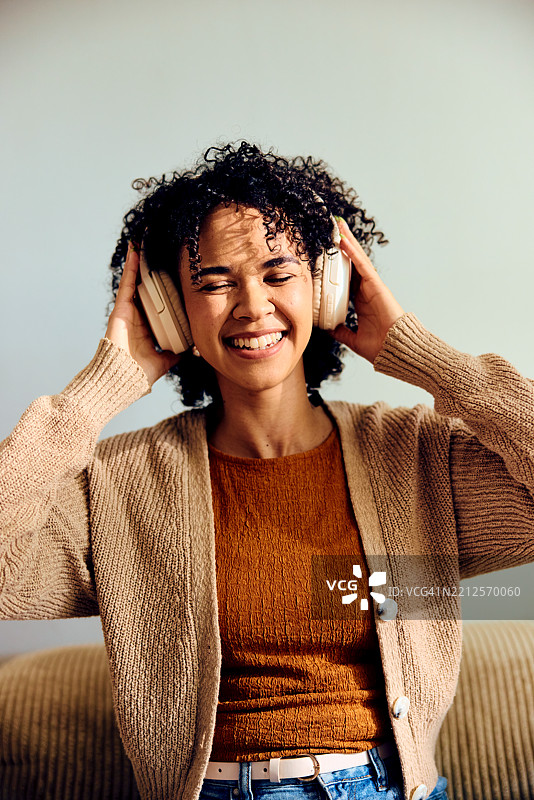 年轻女性在家中戴着耳机，闭着眼睛微笑着听音乐图片素材