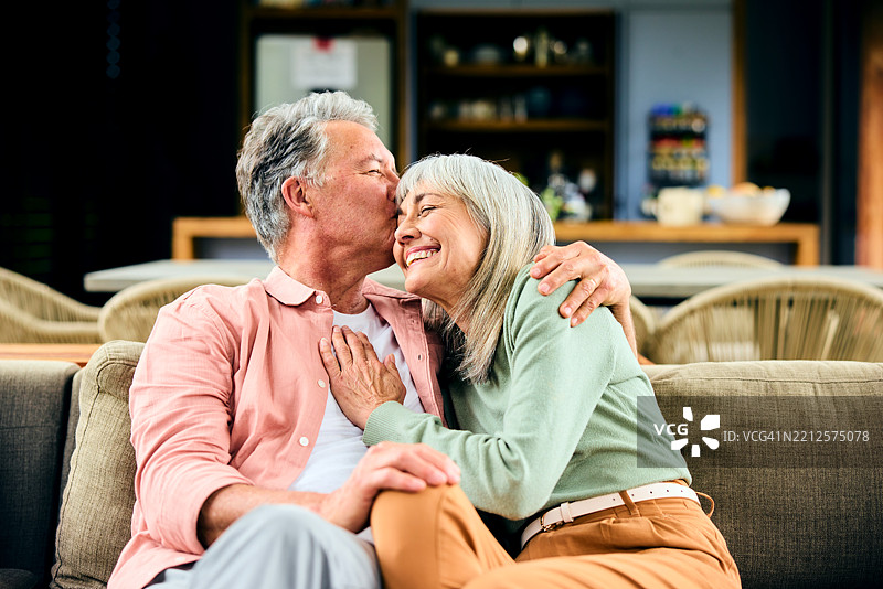 温馨的老年夫妇在家中的沙发上，男人亲吻女人的脸颊图片素材