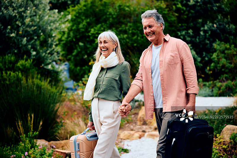 快乐的老年夫妇手牵手走路，提着行李，抵达度假目的地图片素材