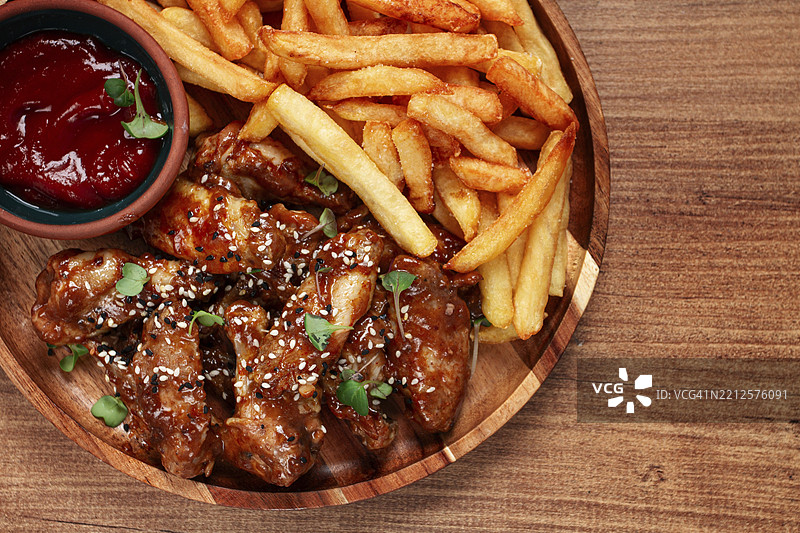 木质盘子上的乡村风格烧烤鸡翅，撒上芝麻，配有薯条和酱汁图片素材
