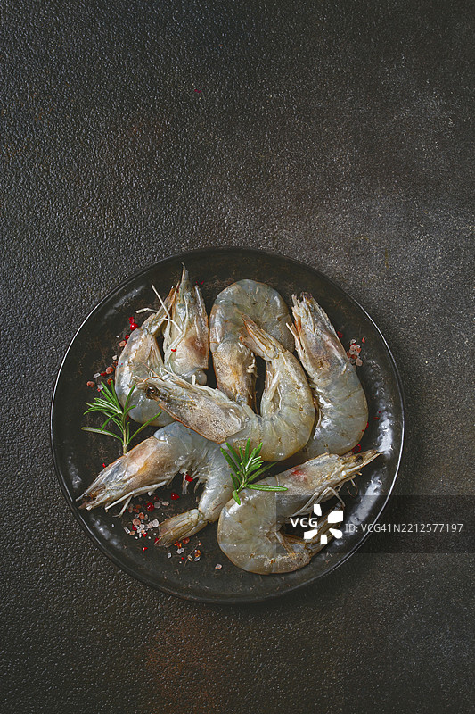 新鲜生的白脚虾和虎虾，放在黑色盘子上，配有香料和草药图片素材