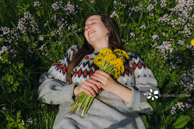 穿着毛衣的宁静女性手捧花束，欣赏春天的花海图片素材