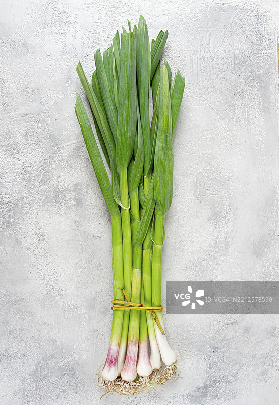 一束年轻的绿色大蒜，放在浅色桌子上，俯视图，无人。图片素材