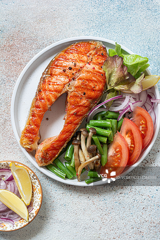 美味的熟三文鱼排，旁边配有鳟鱼、蔬菜、蘑菇和沙拉。健康饮食的理念。图片素材