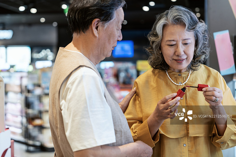 亚洲老年夫妇在购物中心购买口红。图片素材
