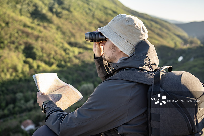 穿着户外装备的探险者正在用地图和望远镜观察山景图片素材