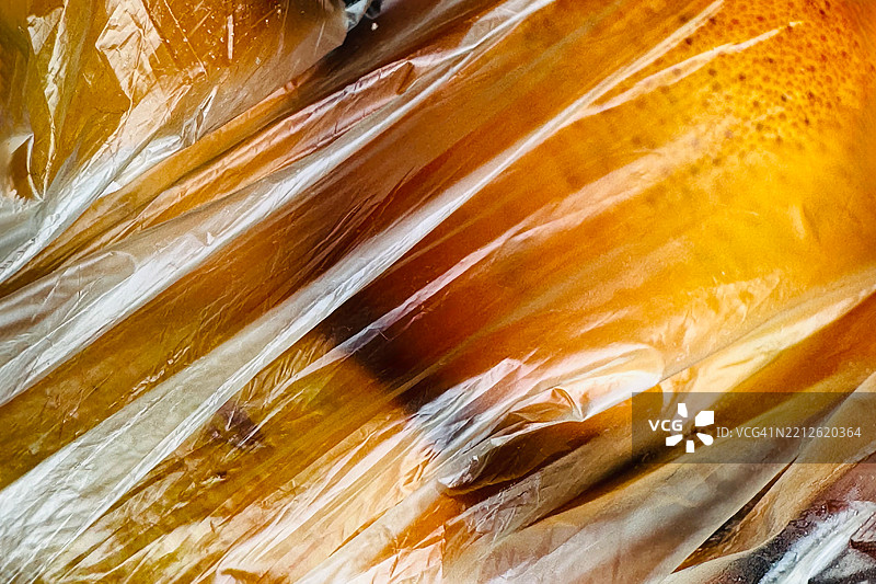 透明塑料薄膜覆盖橙子，形成抽象的纹理背景图片素材