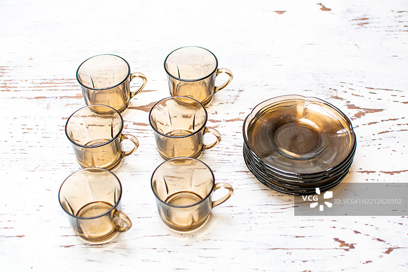 六个棕色咖啡杯和碟子放在白色磨损的木桌上图片素材
