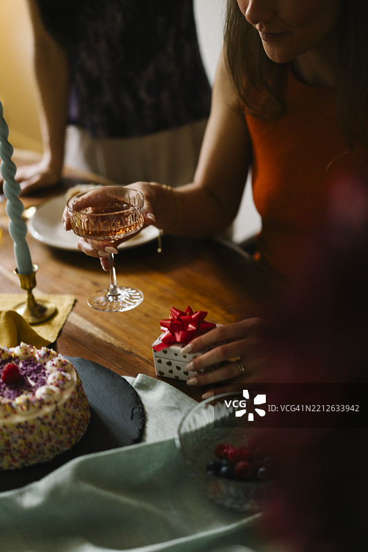 透过生日桌上的模糊物体看去，旁边坐着一个手握香槟杯的人。图片素材