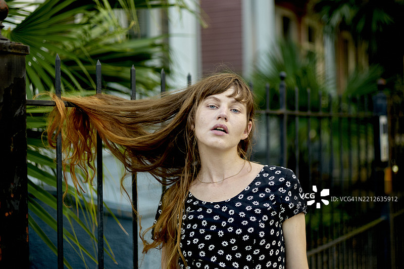 长发女子站在栅栏旁，头发被卡住，穿着花卉图案的上衣，身处户外环境。美国路易斯安那州新奥尔良。图片素材