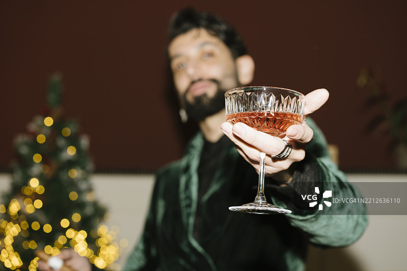 前景中有一个美丽的玻璃杯，杯子被一个模糊的人握着，背景中还有一棵圣诞树。图片素材