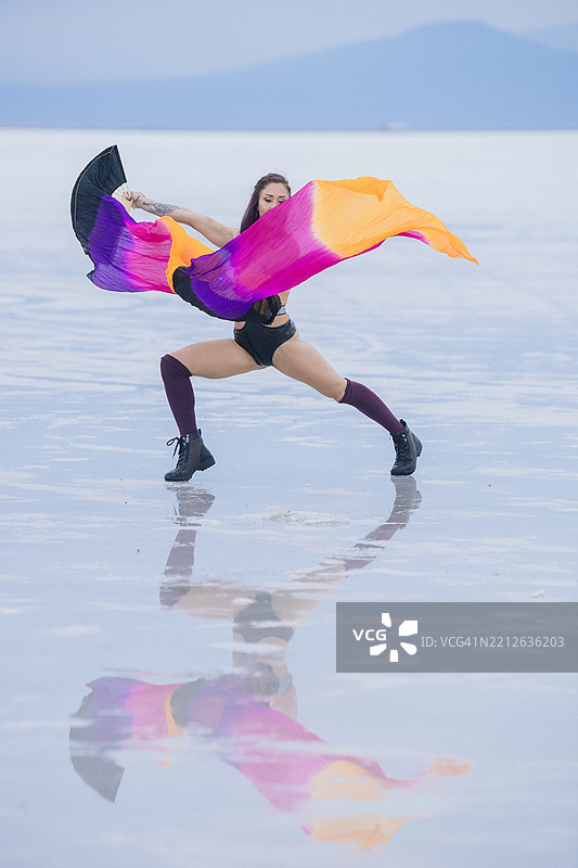 身着鲜艳服装的舞者在反射的盐滩上表演，背景是山脉。博内维尔盐滩，犹他州，美国图片素材