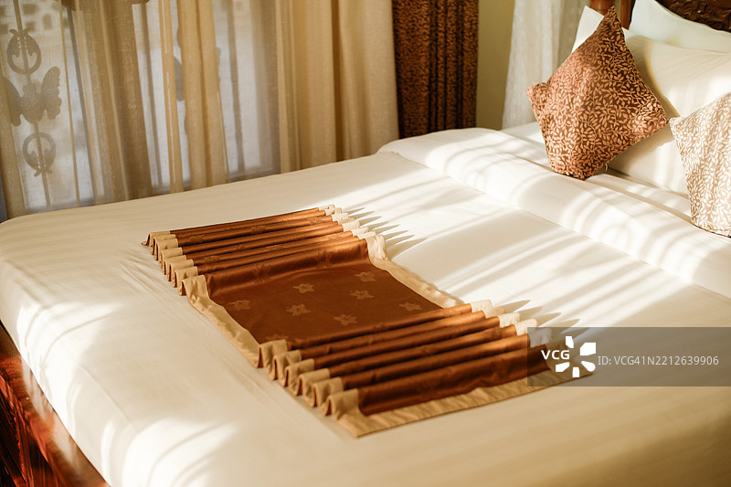 阳光照耀下的酒店床，铺有折叠的装饰跑垫和枕头。坦桑尼亚，非洲图片素材