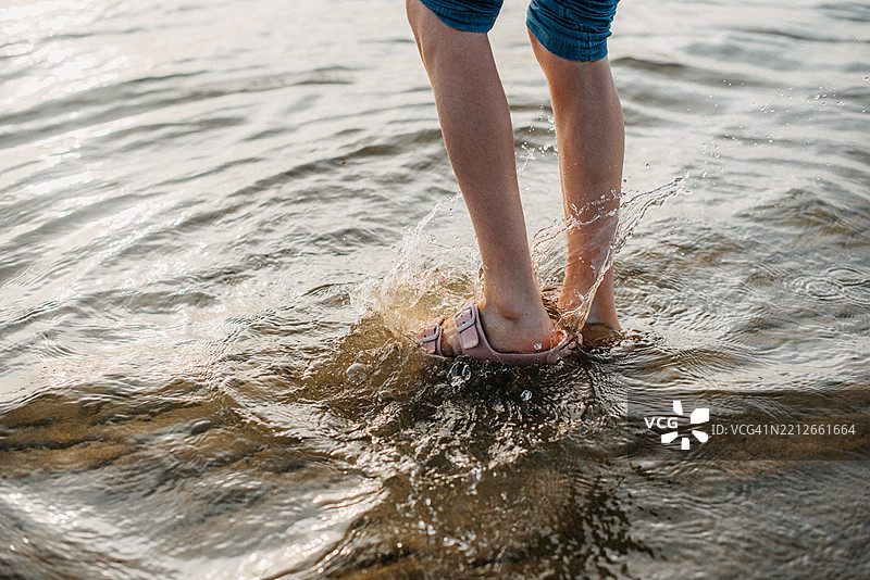 脚在浅水中溅起水花，暗示着海岸边无忧无虑、充满玩乐的时刻。图片素材