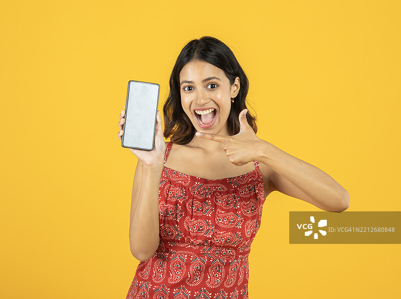 快乐的女人在黄色背景下展示智能手机图片素材