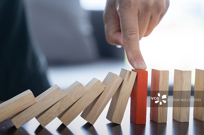商人用手阻止在商业危机管理概念图中倒下的多米诺骨牌，战略与规划概念，木块，商业风险。图片素材