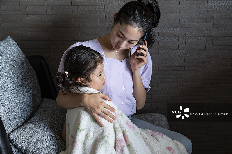 母亲在家照顾生病的女儿，同时打电话给医生。图片素材