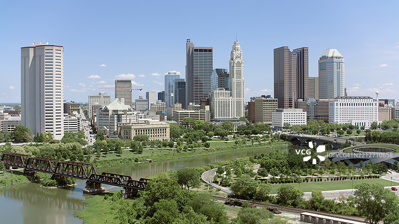乔治亚州哥伦布市中心天际线，阳光明媚的日子里绿意盎然的公园和历史悠久的铁路桥图片素材