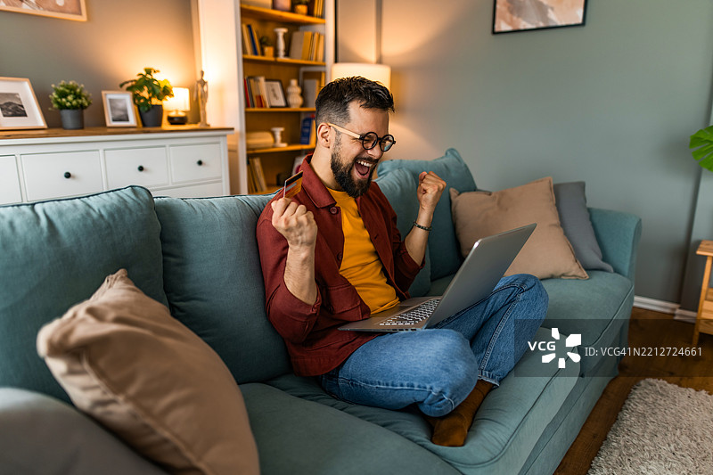 兴奋的男人在家用信用卡网上购物。图片素材