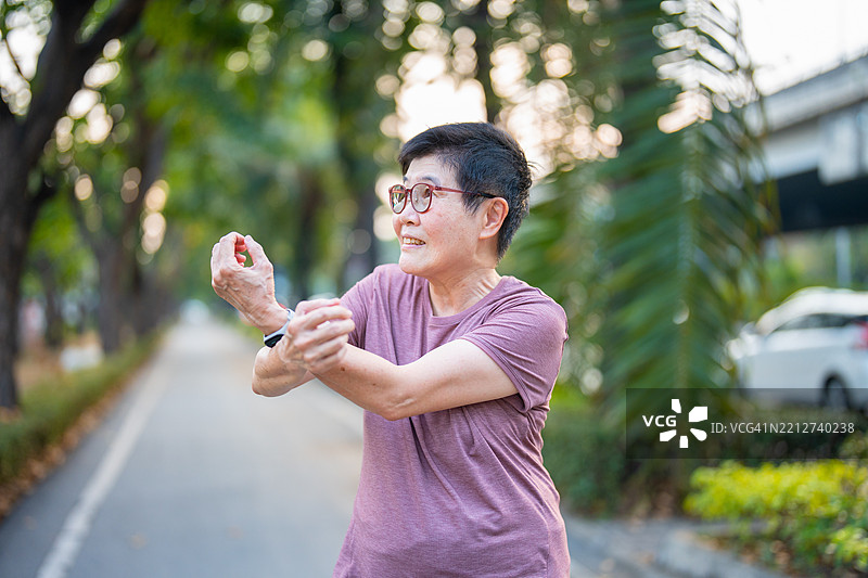 一位老年女性在公园里伸展身体，准备慢跑。图片素材